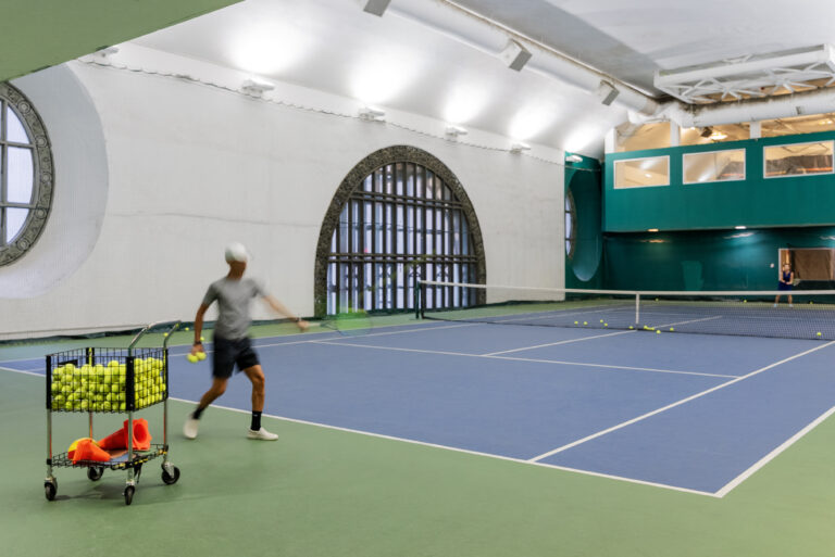 A man is playing tennis in an indoor court.