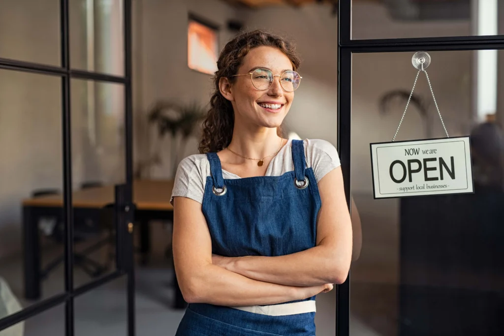 A smiling woman standing in front of an open sign.