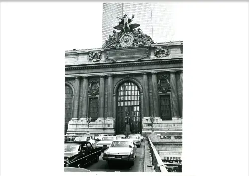 A black and white photo of a building with cars in front of it.