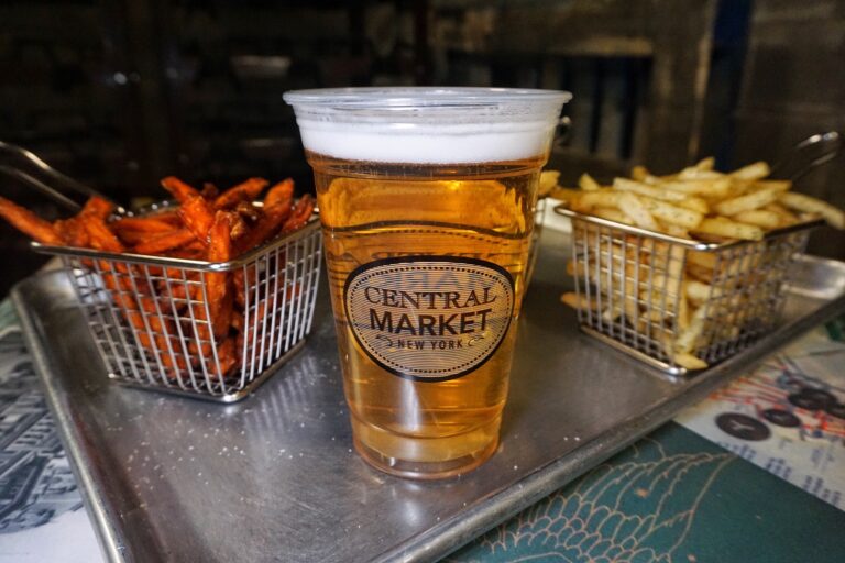 A glass of beer next to a tray of fries.
