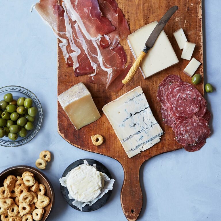 A cutting board with various cheeses, olives and crackers.