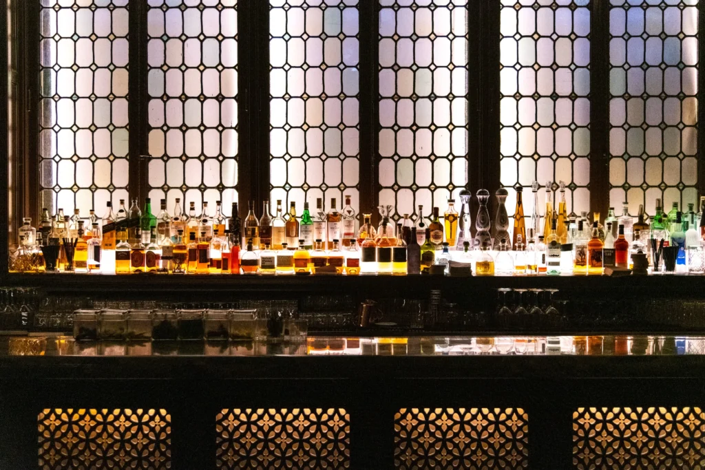 A bar with many bottles in front of a stained glass window.