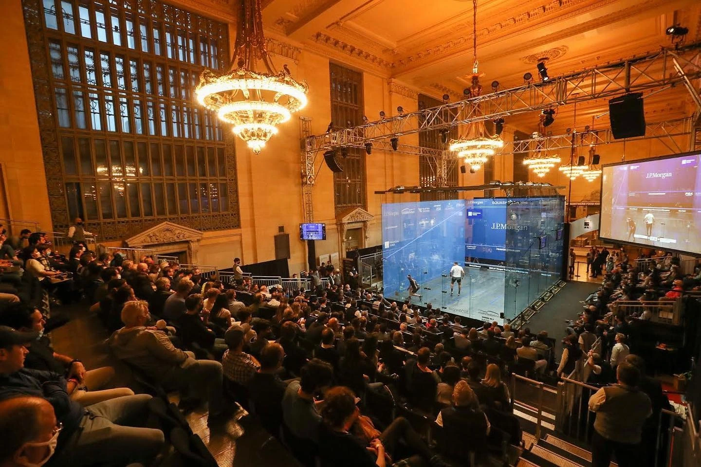 A crowd of people watching a squash match in a large building.