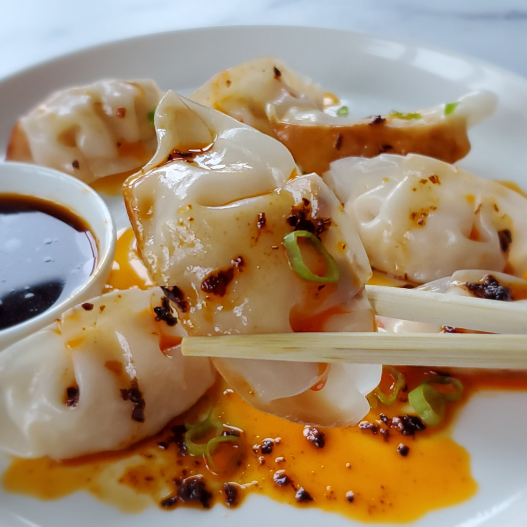 Dumplings with sauce and chopsticks on a plate.