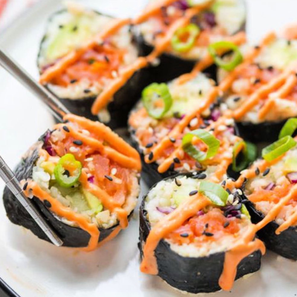 A plate of sushi rolls with sauce and toppings.