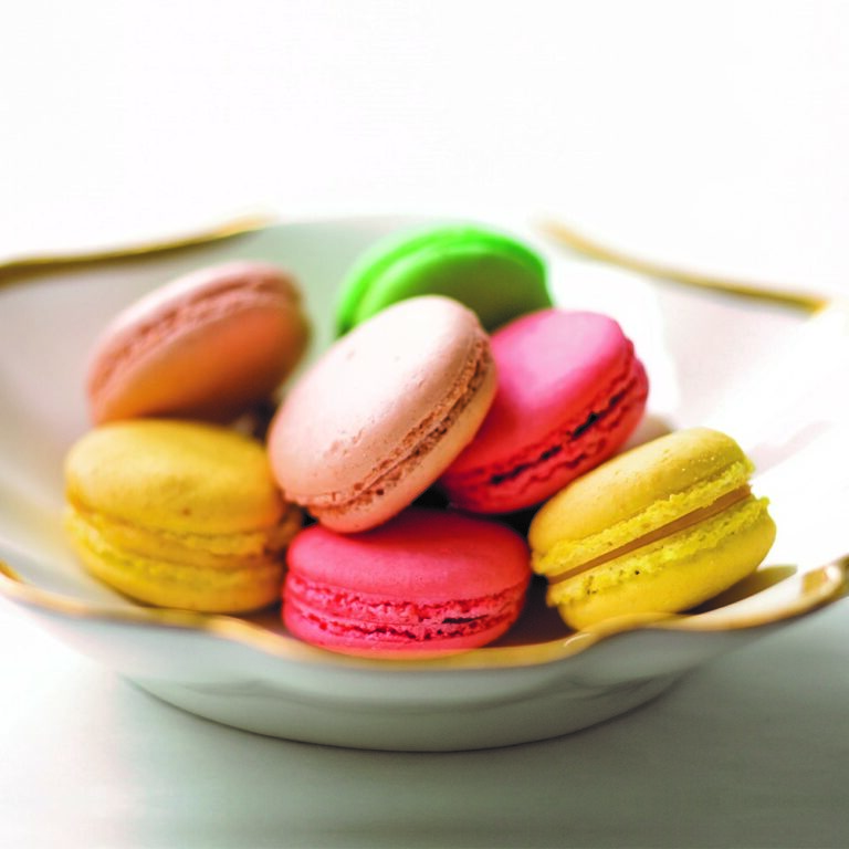 Colorful macarons in a white bowl.