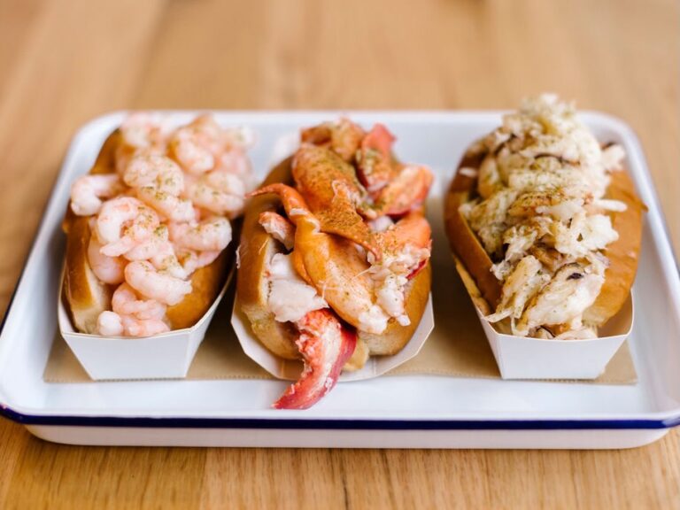 Three hot dogs on a tray with shrimp and lobster.