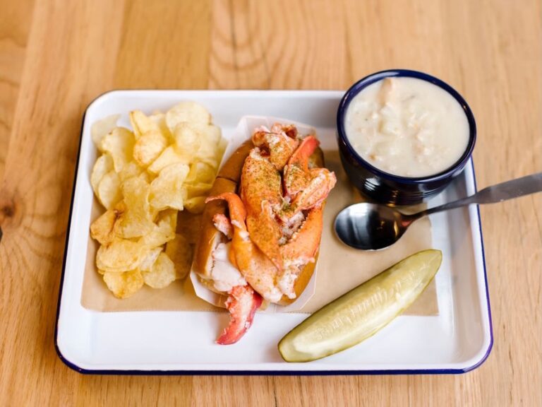 A lobster roll and potato chips on a plate.
