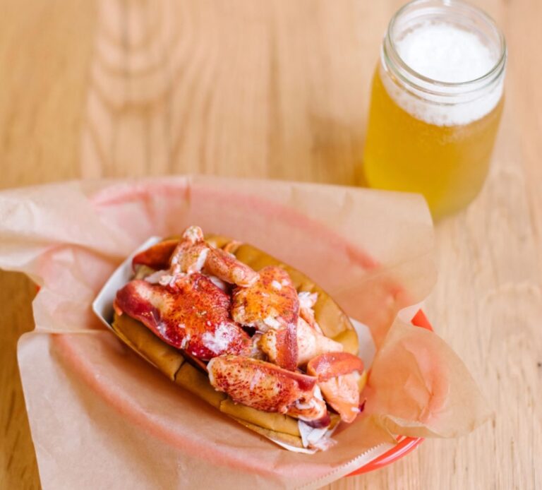 A lobster hot dog is sitting on a table next to a glass of beer.